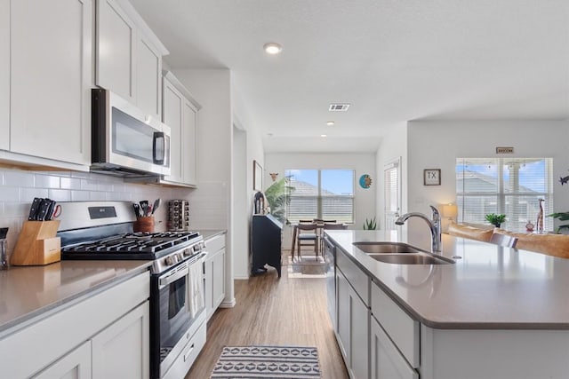 kitchen featuring visible vents, decorative backsplash, light wood-style floors, stainless steel appliances, and a sink