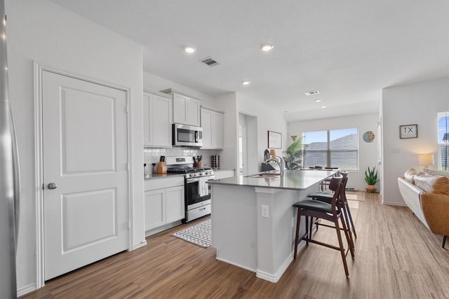 kitchen featuring visible vents, open floor plan, an island with sink, appliances with stainless steel finishes, and a sink