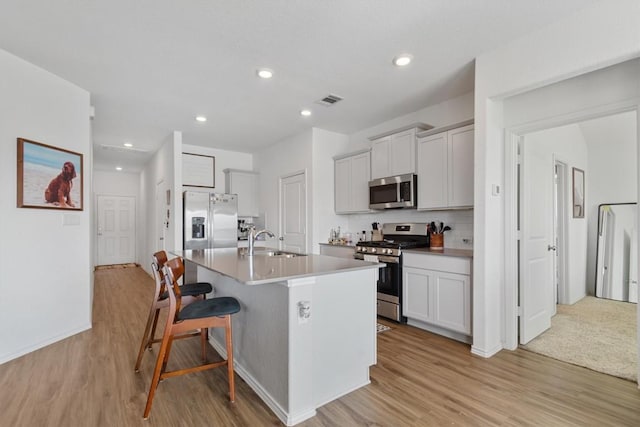 kitchen with visible vents, an island with sink, a sink, stainless steel appliances, and a kitchen bar