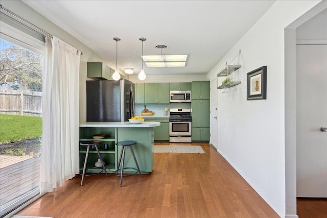 kitchen with wood finished floors, visible vents, a peninsula, stainless steel appliances, and green cabinets