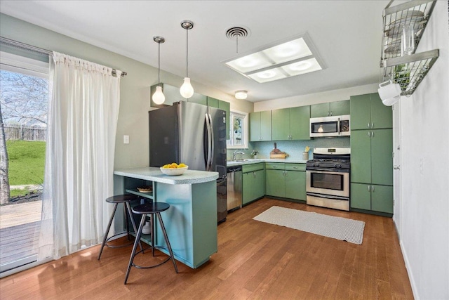 kitchen with appliances with stainless steel finishes, green cabinets, a peninsula, and wood finished floors