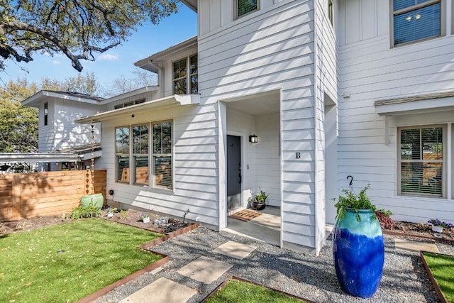 entrance to property featuring a lawn, board and batten siding, and fence