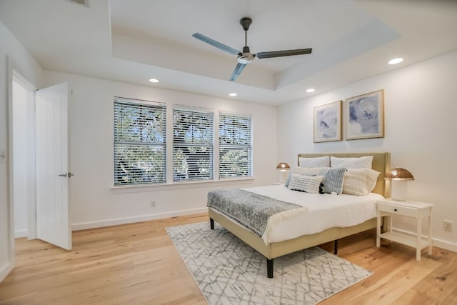 bedroom featuring a raised ceiling, light wood-style flooring, recessed lighting, and baseboards