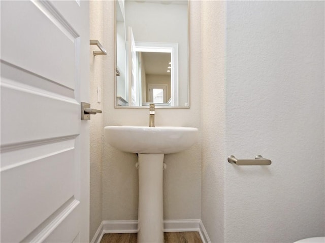 bathroom with baseboards, wood finished floors, and a textured wall