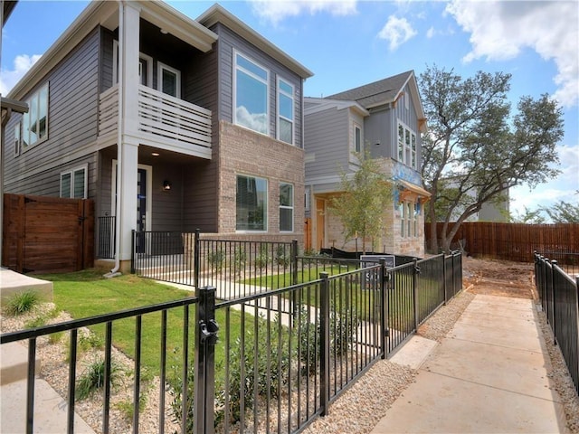 view of front of home with a balcony, a gate, a fenced backyard, a front lawn, and brick siding