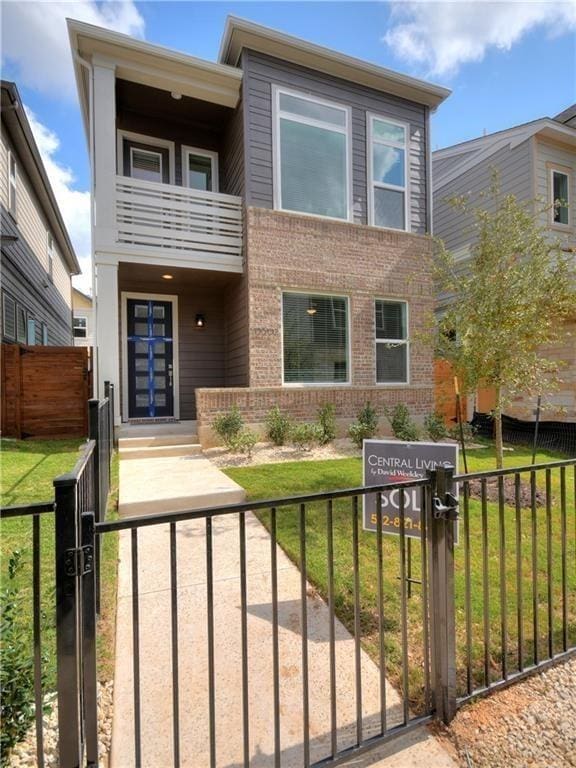 view of front of house featuring a fenced front yard, a front yard, a balcony, and brick siding