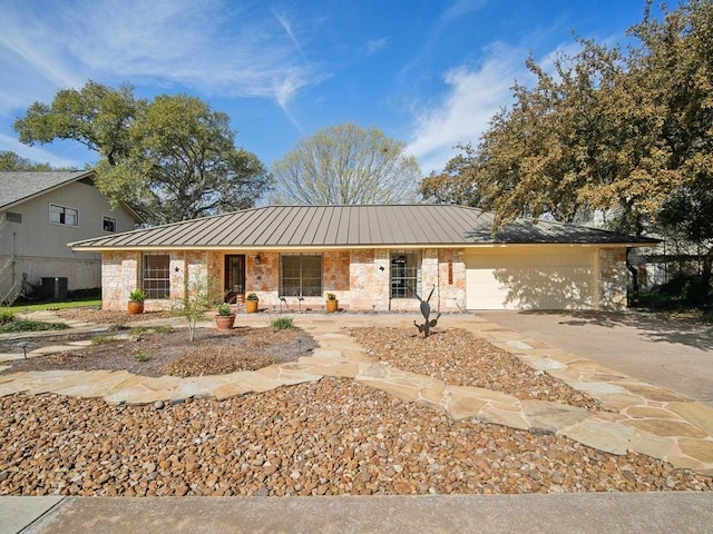 single story home featuring central air condition unit, stone siding, concrete driveway, an attached garage, and metal roof