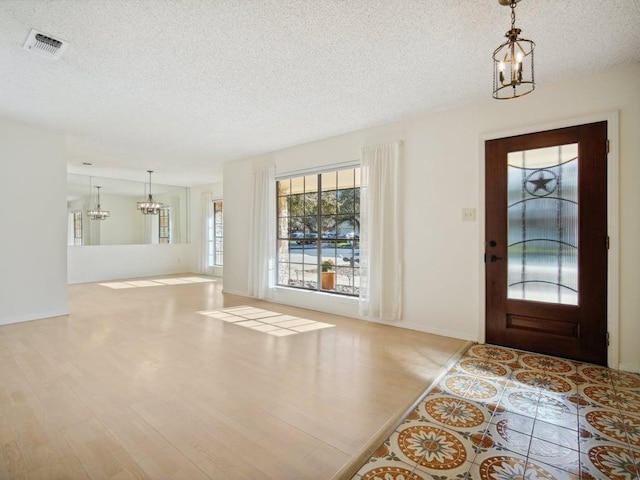 foyer entrance featuring visible vents, a notable chandelier, a textured ceiling, wood finished floors, and baseboards