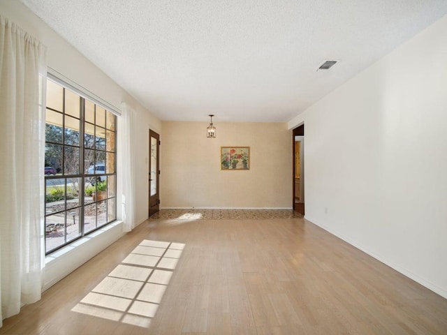 unfurnished room with a textured ceiling, baseboards, visible vents, and light wood-type flooring