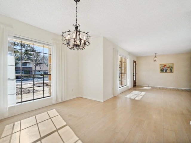 unfurnished dining area with a textured ceiling, baseboards, light wood-type flooring, and a chandelier