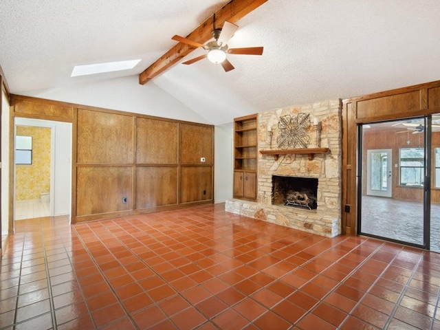 unfurnished living room with vaulted ceiling with skylight, a textured ceiling, a stone fireplace, and a ceiling fan