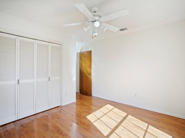 unfurnished bedroom with visible vents, ceiling fan, baseboards, wood finished floors, and a closet