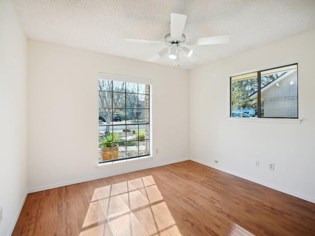 empty room with a wealth of natural light, a textured ceiling, wood finished floors, and ceiling fan