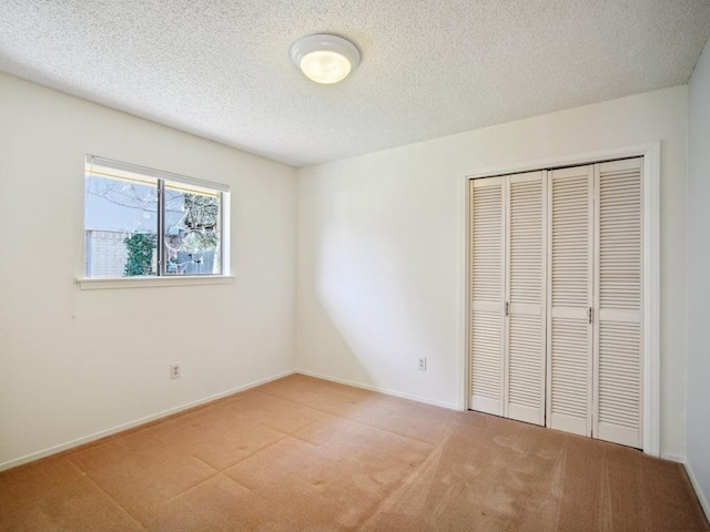 unfurnished bedroom with light carpet, baseboards, a textured ceiling, and a closet