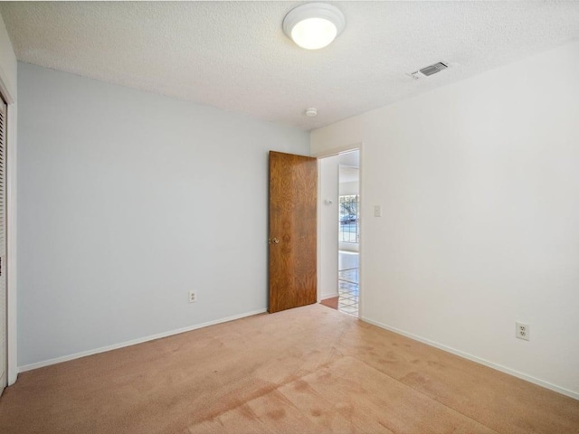 unfurnished room with a textured ceiling, baseboards, visible vents, and light carpet