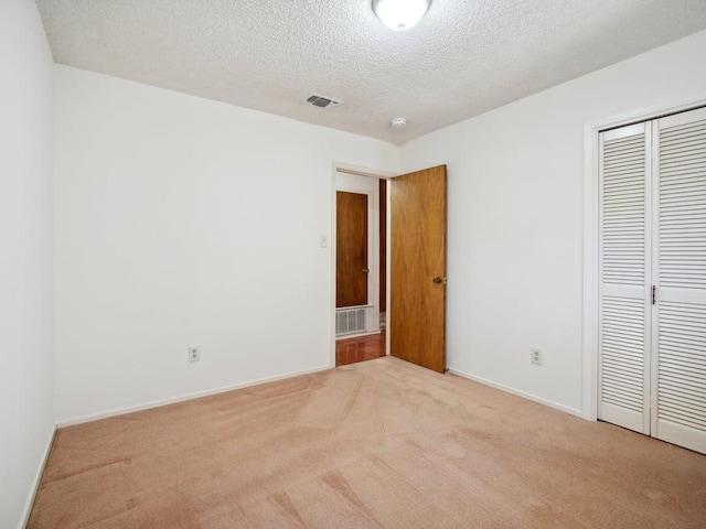 unfurnished bedroom featuring light colored carpet, visible vents, a closet, and a textured ceiling