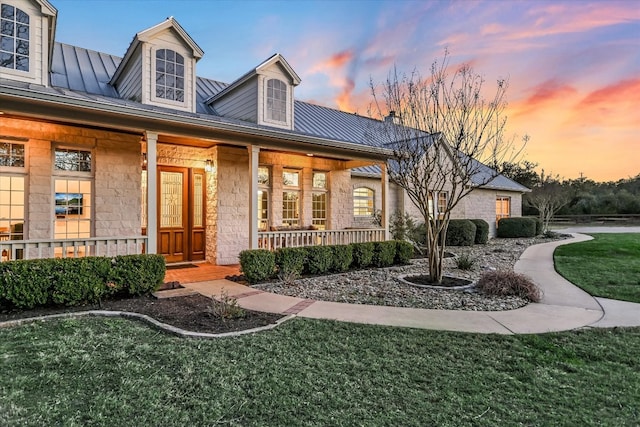 view of front facade featuring metal roof, stone siding, covered porch, and a standing seam roof