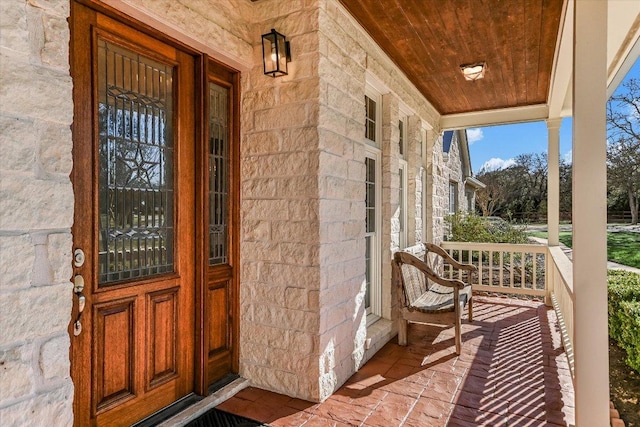 doorway to property with a porch and stone siding