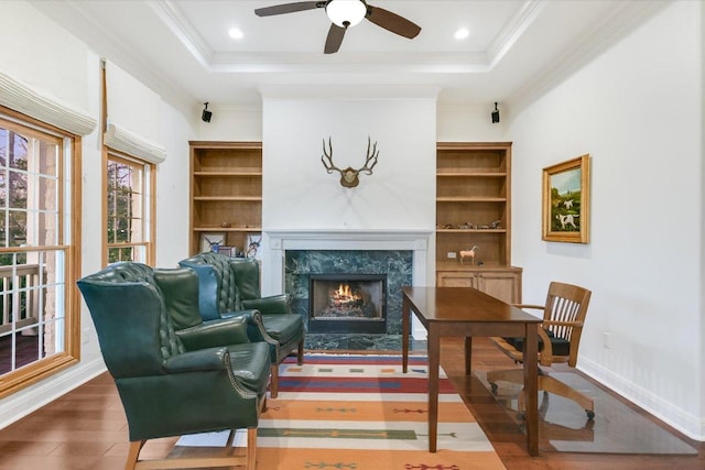 living area with a ceiling fan, wood finished floors, a high end fireplace, crown molding, and a raised ceiling