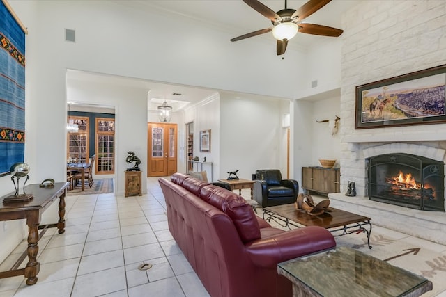 living room featuring a ceiling fan, light tile patterned flooring, a fireplace, a towering ceiling, and crown molding