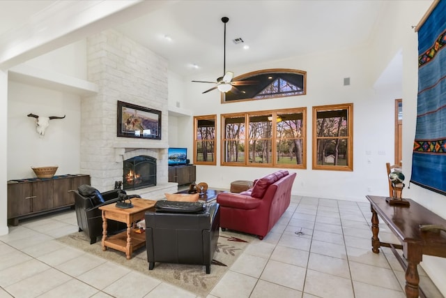 living room with visible vents, a high ceiling, a stone fireplace, light tile patterned flooring, and ceiling fan