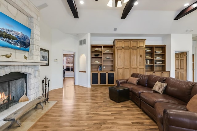 living area featuring visible vents, baseboards, beamed ceiling, a fireplace, and light wood-style floors