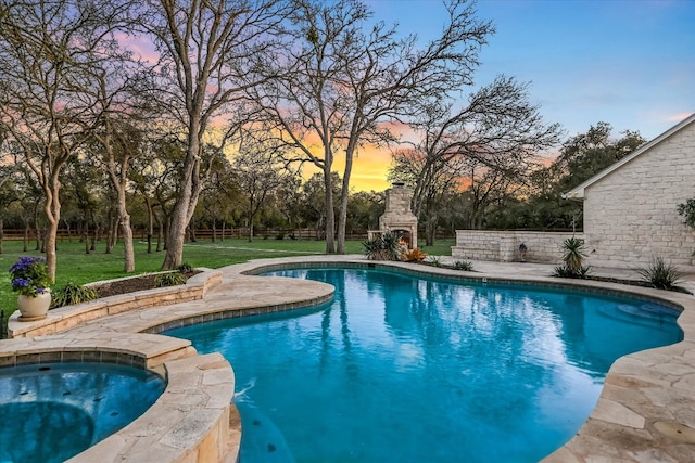 view of swimming pool with a pool with connected hot tub, fence, a lawn, an outdoor fireplace, and a patio area