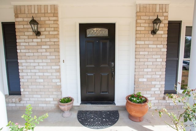 view of exterior entry with brick siding and a porch