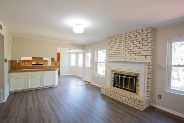 unfurnished living room with visible vents, baseboards, a brick fireplace, and dark wood finished floors