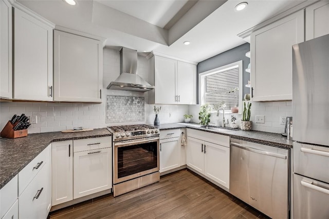 kitchen with dark wood-type flooring, a sink, white cabinetry, stainless steel appliances, and wall chimney range hood