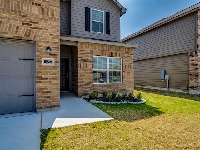 entrance to property featuring a garage, a yard, and brick siding