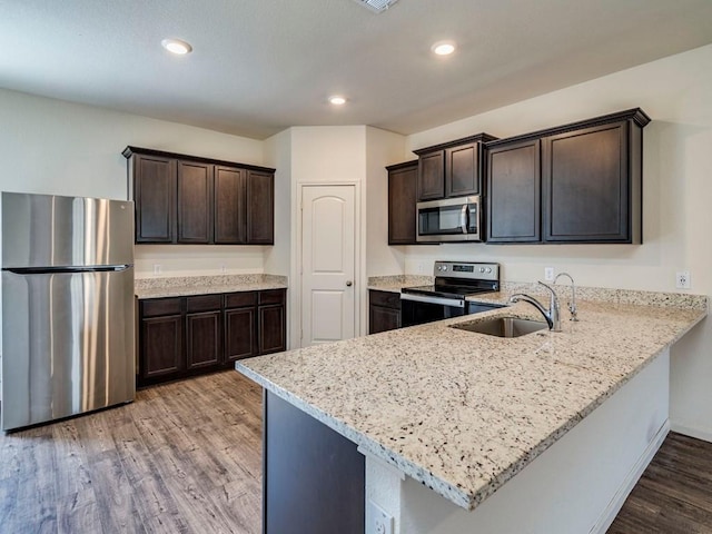 kitchen with dark brown cabinets, stainless steel appliances, light wood-style flooring, and a sink