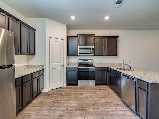 kitchen with visible vents, light wood-style flooring, a sink, stainless steel appliances, and dark brown cabinetry