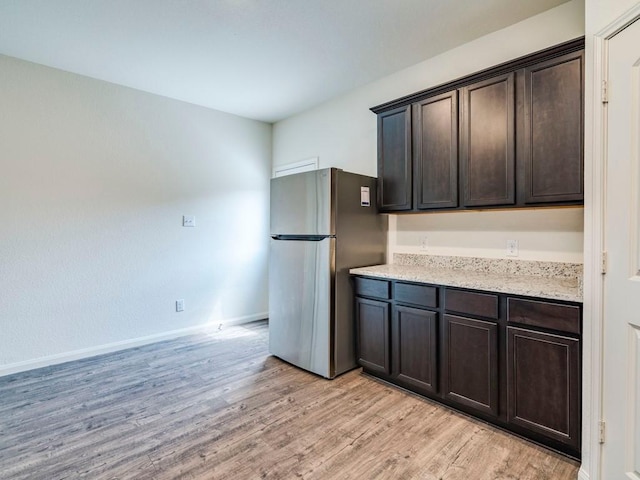 kitchen featuring baseboards, dark brown cabinetry, light stone counters, freestanding refrigerator, and light wood-style floors