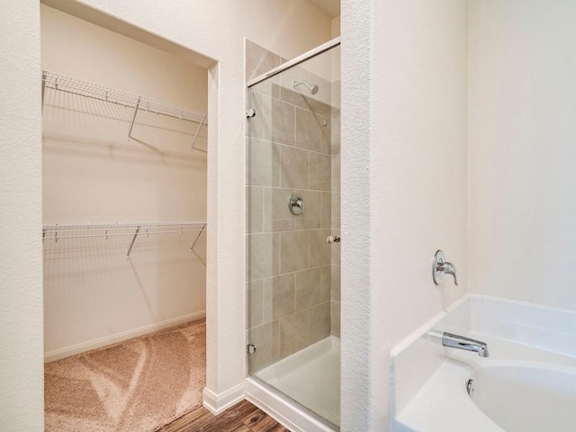 bathroom with a walk in closet, a shower stall, a garden tub, and wood finished floors