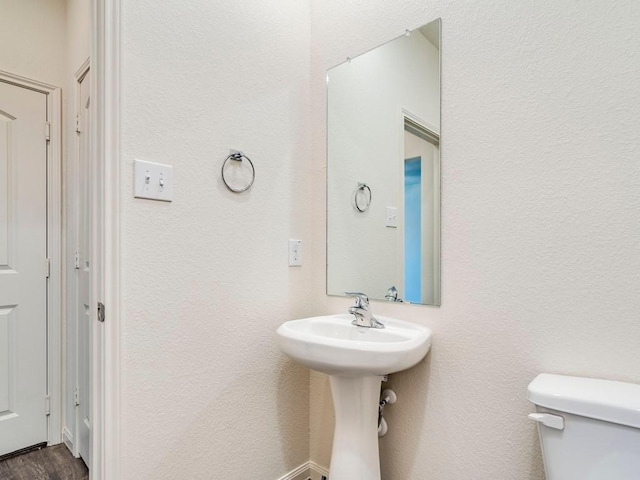 half bathroom featuring toilet, wood finished floors, and a textured wall