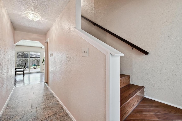 stairs with baseboards, a textured ceiling, stone tile flooring, and a textured wall