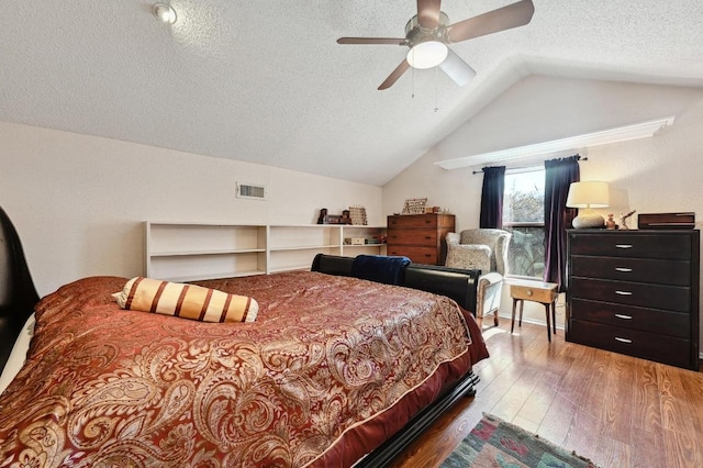 bedroom with visible vents, a textured ceiling, wood finished floors, lofted ceiling, and ceiling fan