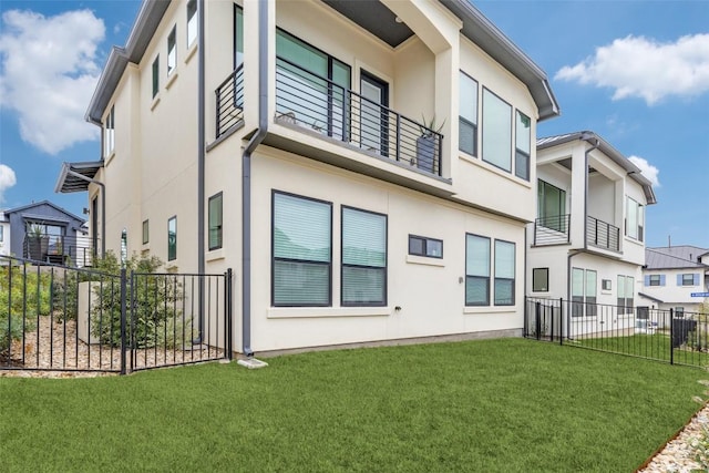 back of house featuring stucco siding, a lawn, a balcony, and fence