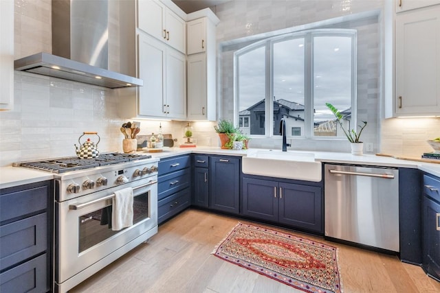 kitchen with a sink, wall chimney range hood, blue cabinets, and stainless steel appliances