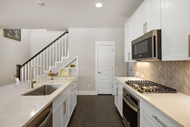 kitchen featuring light stone counters, decorative backsplash, white cabinets, stainless steel appliances, and a sink