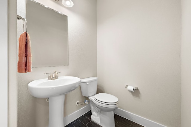 half bathroom with toilet, baseboards, and a sink