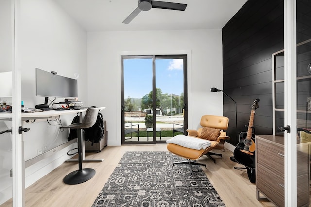 office featuring wooden walls, an accent wall, ceiling fan, and wood finished floors