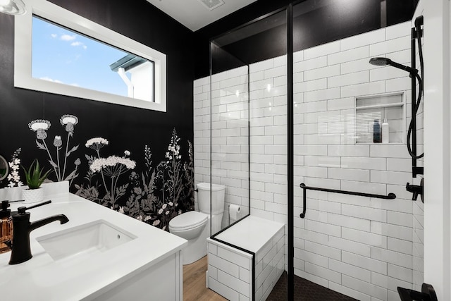 bathroom featuring tiled shower, toilet, wood finished floors, and vanity