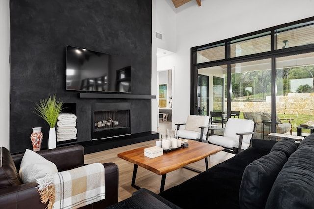 living area with visible vents, a fireplace with raised hearth, a towering ceiling, and wood finished floors