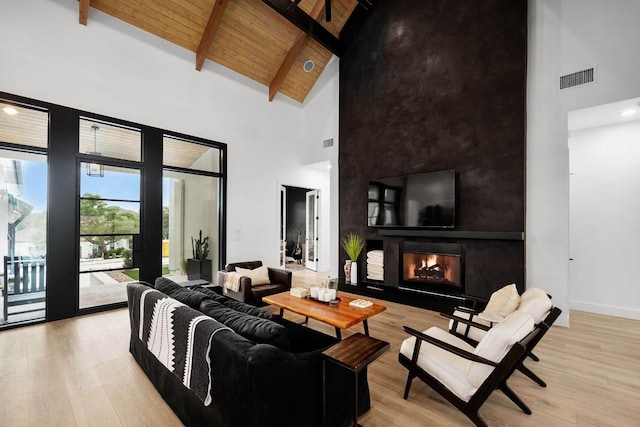 living room with visible vents, beamed ceiling, light wood-style flooring, wooden ceiling, and a warm lit fireplace