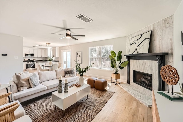 living area with baseboards, visible vents, light wood finished floors, a high end fireplace, and ceiling fan