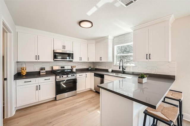 kitchen featuring visible vents, a sink, a kitchen breakfast bar, dark countertops, and stainless steel appliances