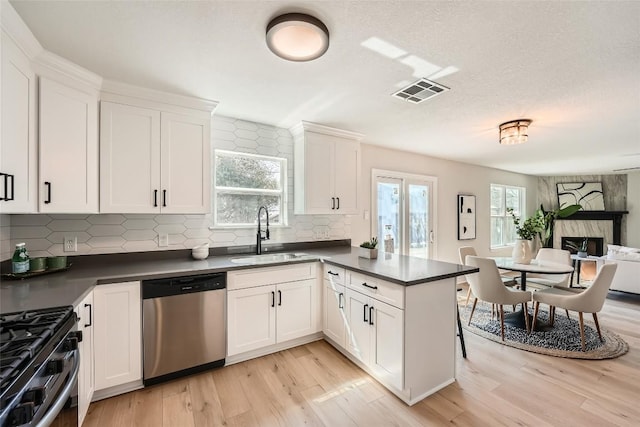 kitchen with a sink, dark countertops, stainless steel appliances, light wood-style floors, and a peninsula