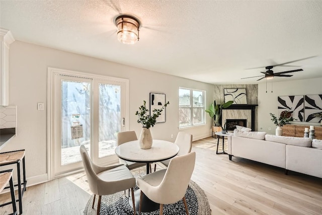 dining room featuring light wood finished floors, a textured ceiling, ceiling fan, and a premium fireplace